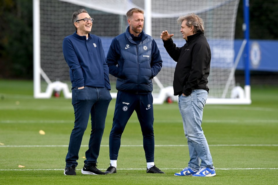 three men standing on a soccer field with one wearing a jacket that says ' chelsea ' on it