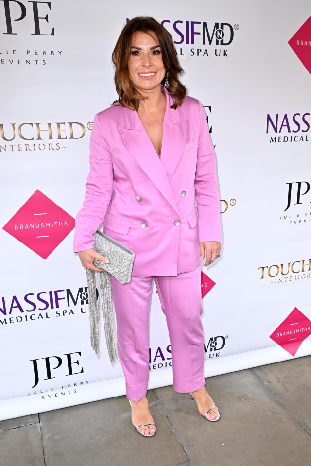 a woman in a pink suit stands in front of a wall that says jpe