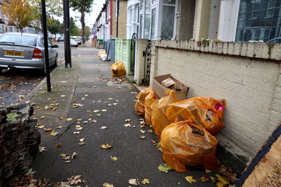 a pile of garbage bags on a sidewalk with a silver car parked behind them