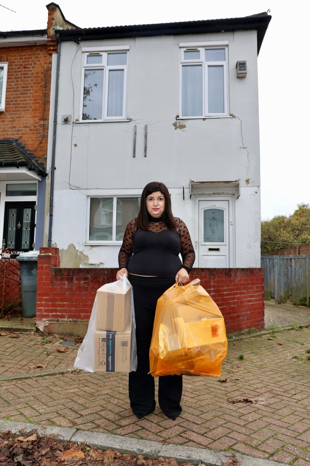 a woman standing in front of a white house holding a bag and boxes from amazon