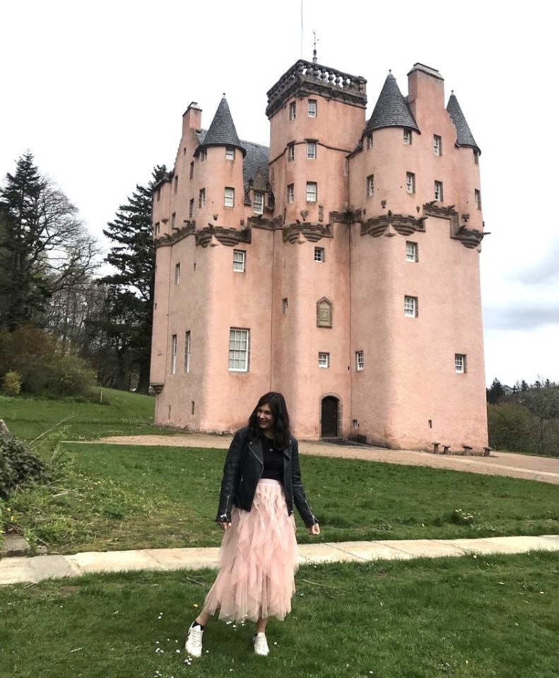 a woman stands in front of a pink castle