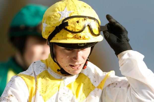 a jockey adjusts his goggles while riding a horse