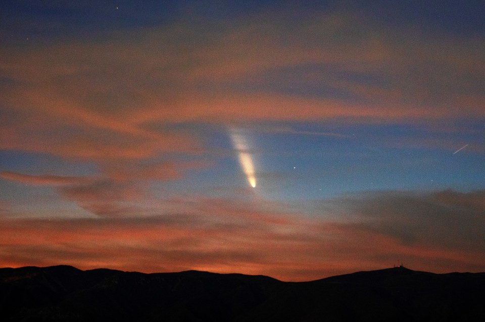 a comet is visible in the night sky above the mountains