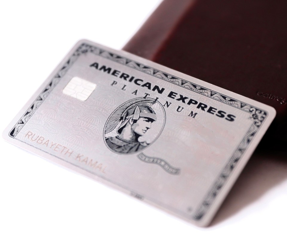 a silver american express platinum card sits on top of a brown wallet