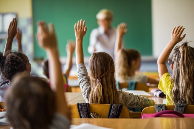 a group of children are raising their hands in a classroom