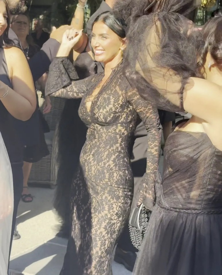 a woman in a black lace dress stands in a crowd of people