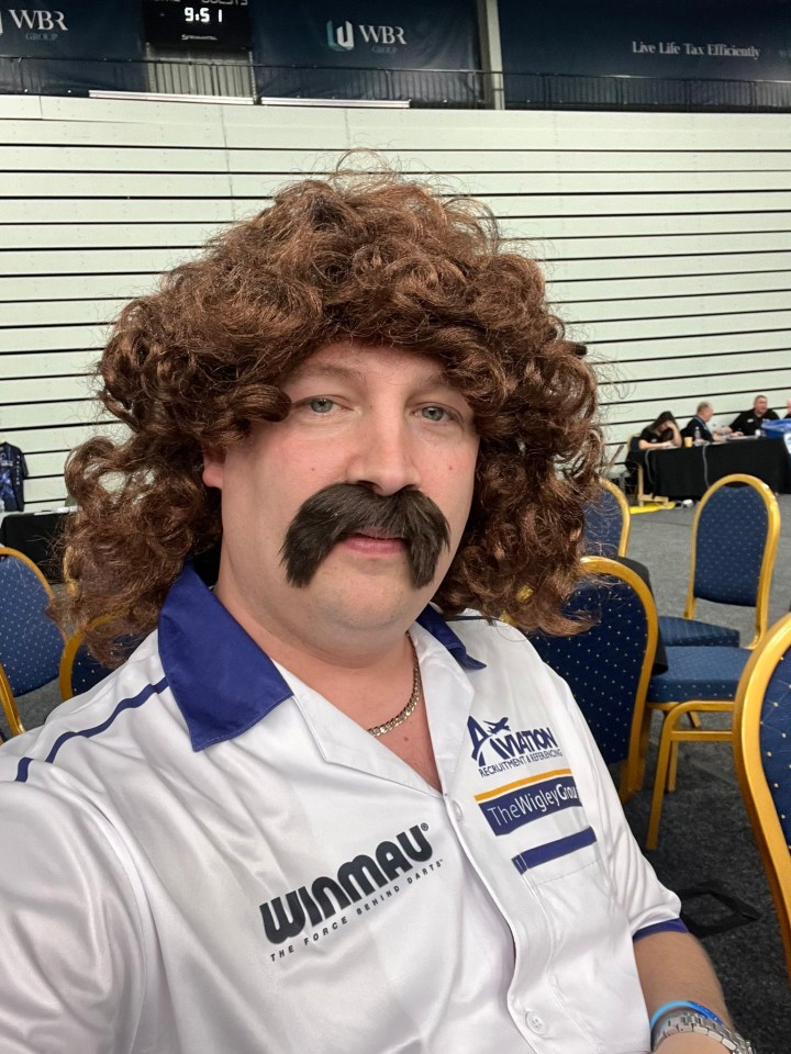 a man with a wig and mustache is wearing a winmau shirt