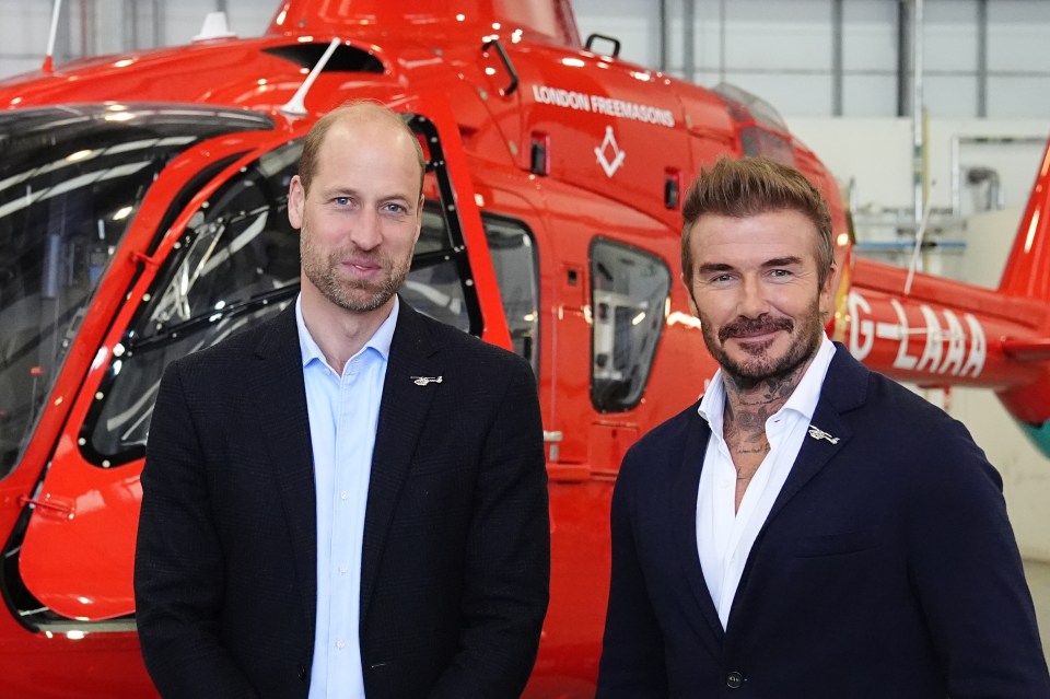 two men stand in front of a red helicopter that says london freemasons