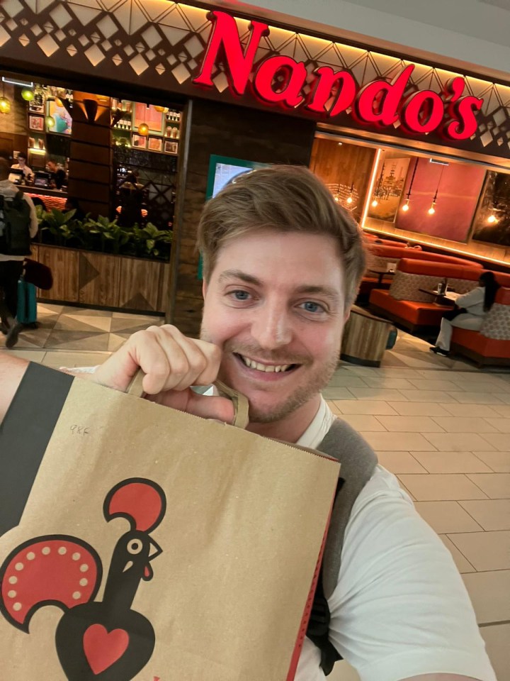 a man holding a bag in front of a nando 's restaurant