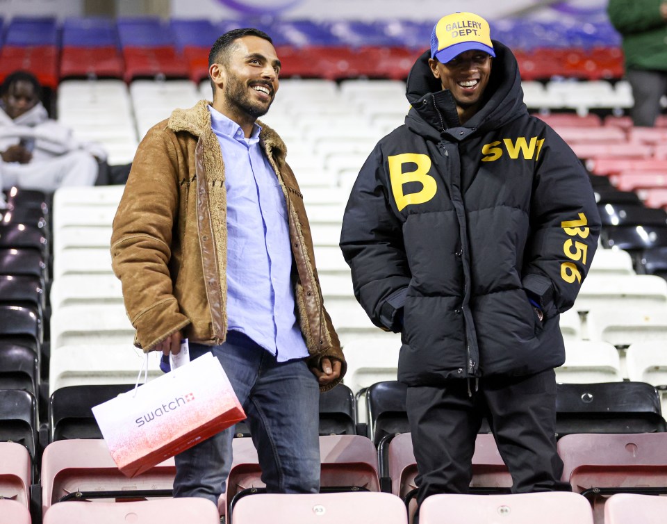 two men standing in a stadium with one wearing a jacket with the letter b on it