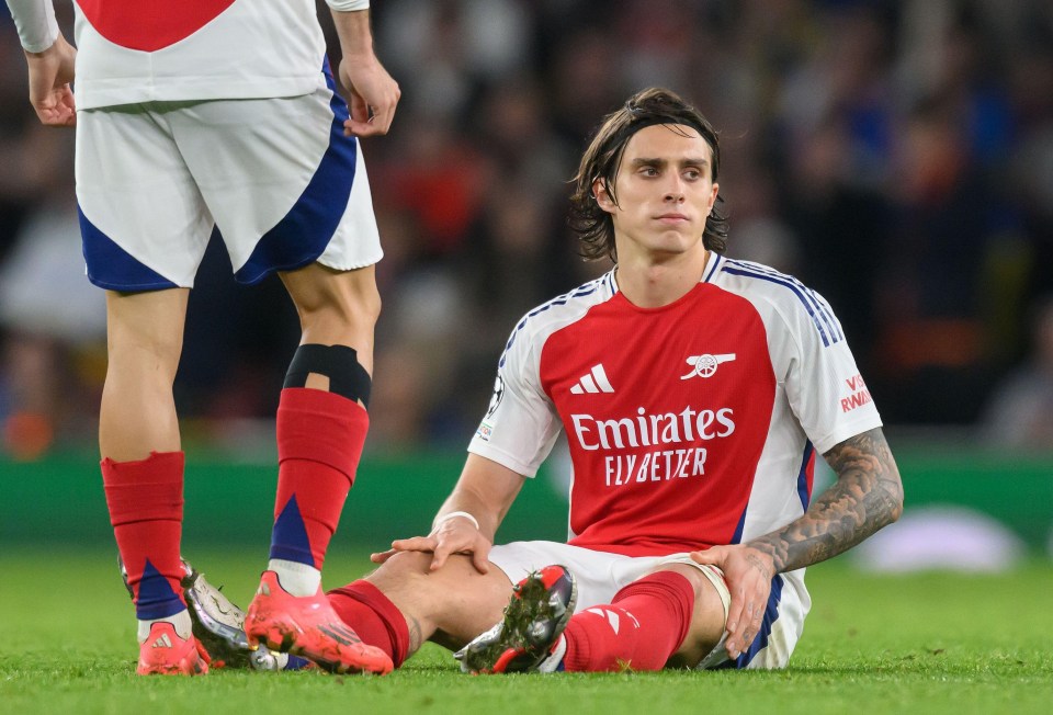 a soccer player wearing an emirates fly better jersey sits on the field