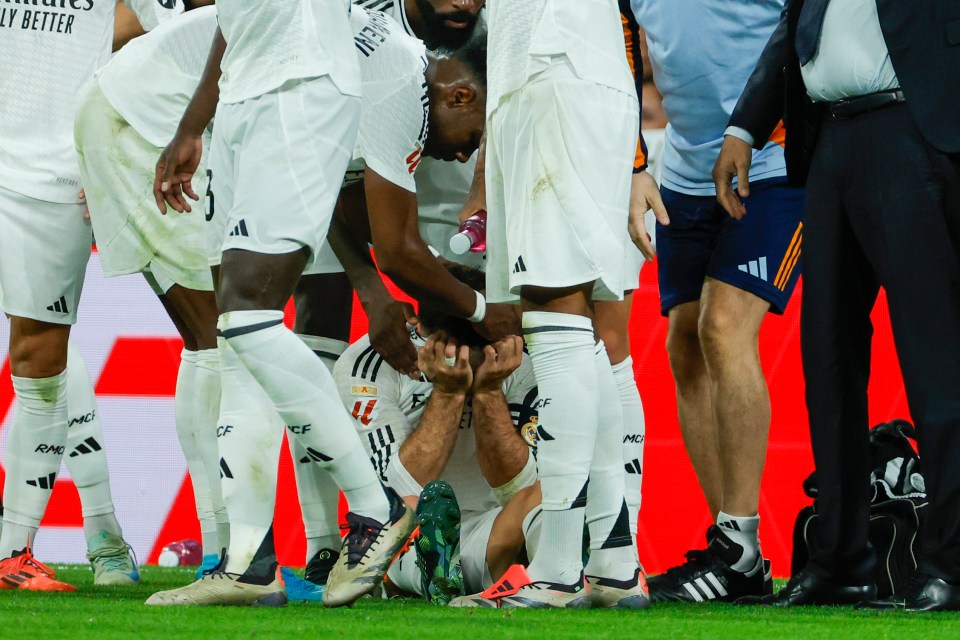 a group of soccer players huddle around a player who is laying on the ground