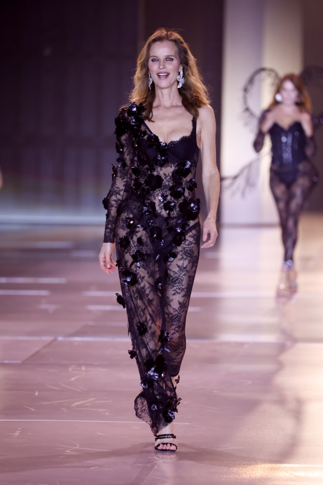 a woman in a black lace dress walks down a runway