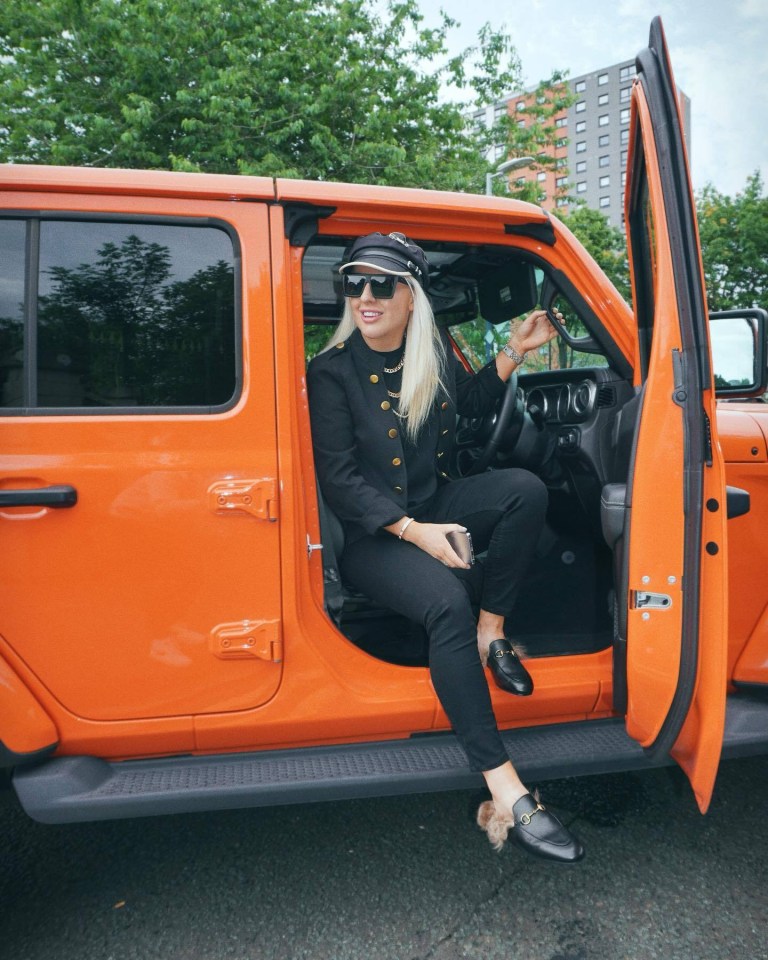 a woman sits in the driver 's seat of an orange jeep