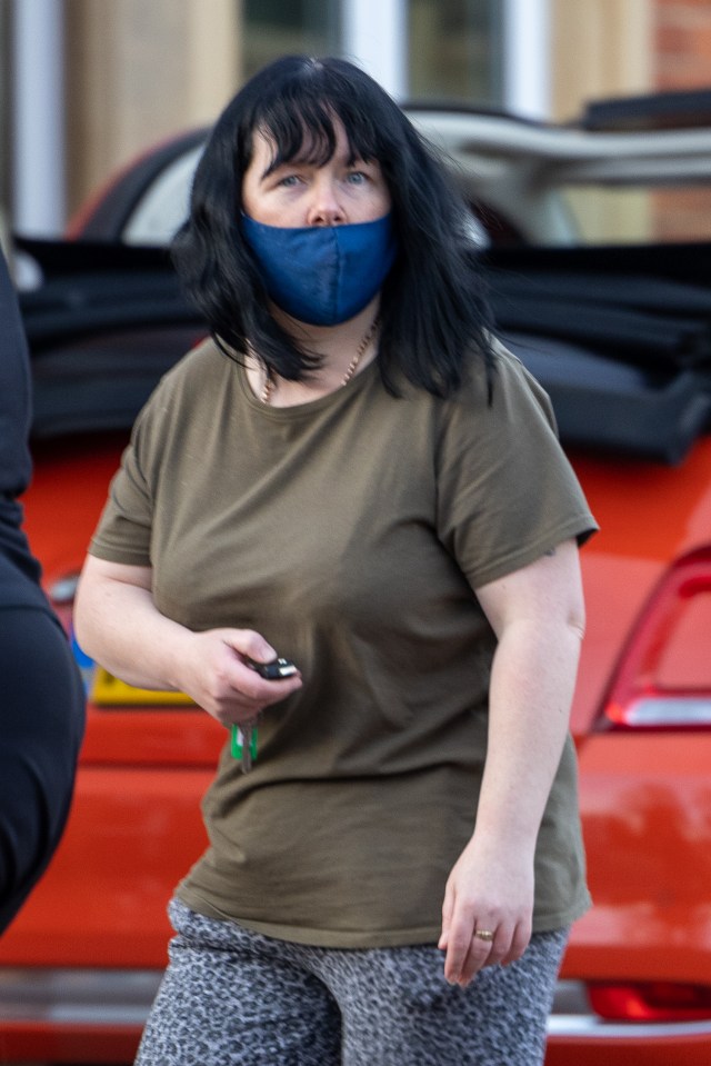 a woman wearing a blue face mask stands in front of an orange car