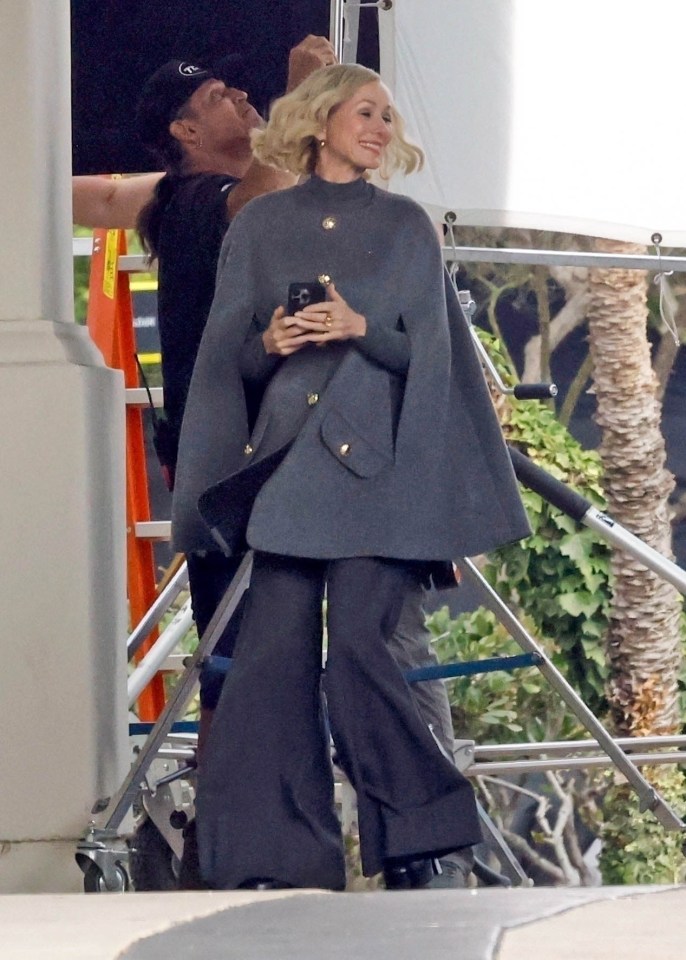 a woman wearing a grey cape holds a cell phone