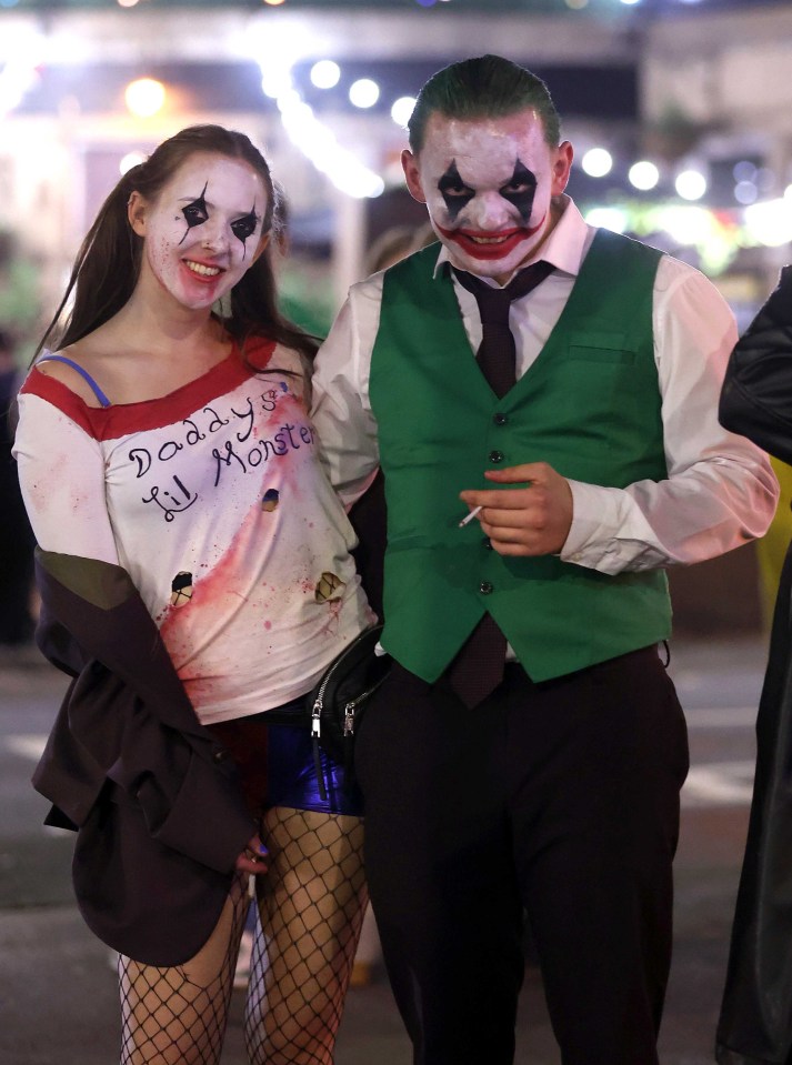 a woman in a daddy 's lil monster shirt stands next to a man in a joker costume