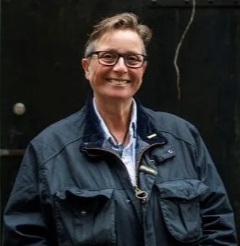 a woman wearing glasses and a black jacket is smiling in front of a black door .