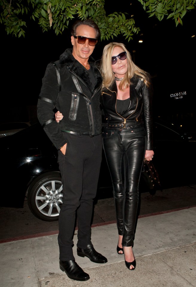 a man and a woman pose for a photo on a sidewalk with a car parked in the background