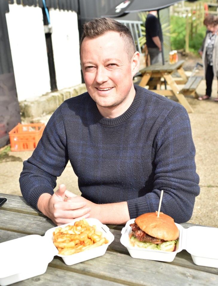 a man sits at a picnic table with a hamburger and french fries