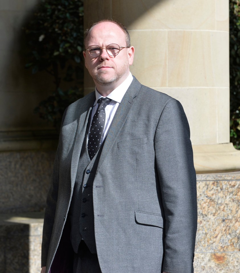 a man in a suit and tie stands in front of a stone wall