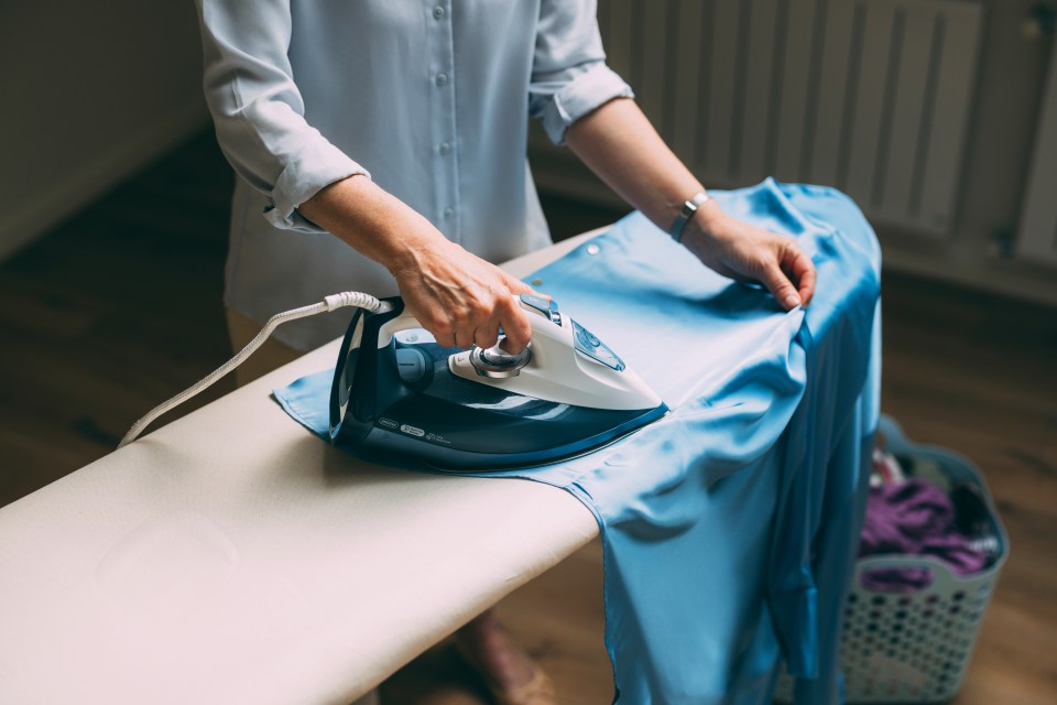 a woman is ironing a blue shirt on an ironing board