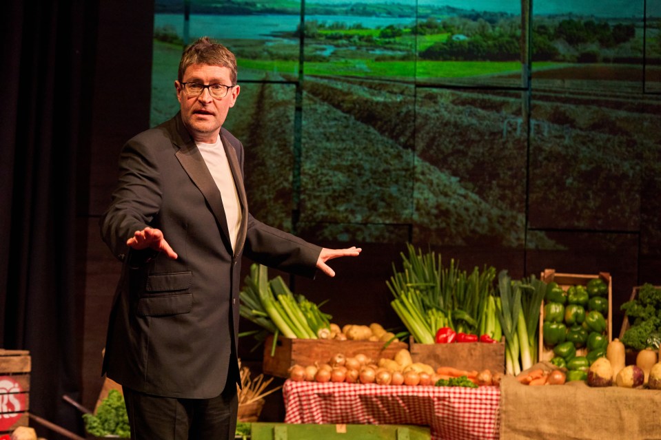 a man in a suit stands in front of a table full of vegetables