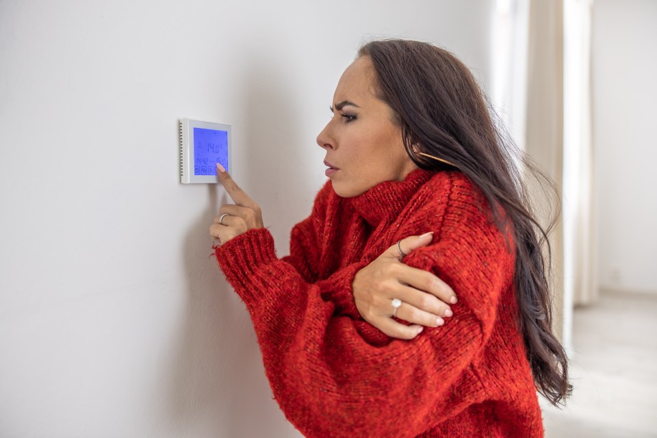 a woman in a red sweater is adjusting a thermostat