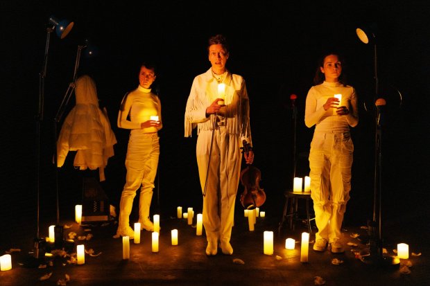 three people in white holding candles in a dark room