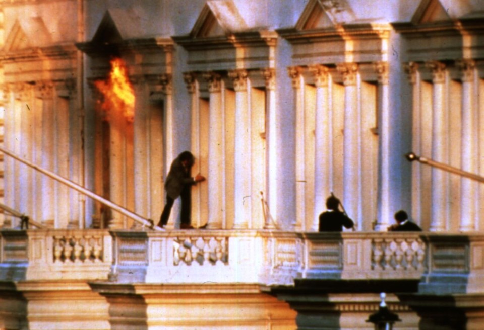 a man standing on a balcony with a fire behind him