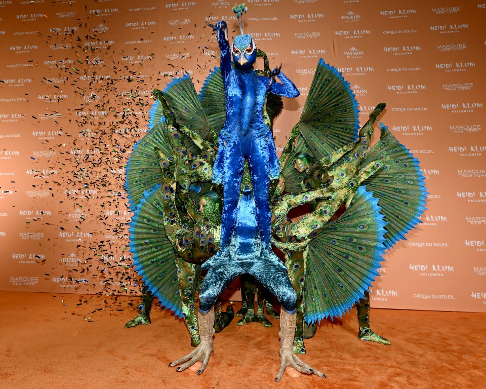 a group of people dressed in peacock costumes are standing in front of a wall that says heidi klum