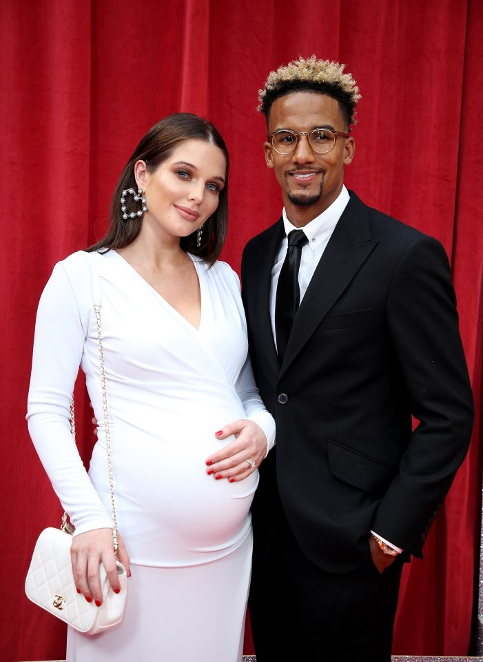 a man in a suit stands next to a pregnant woman in a white dress