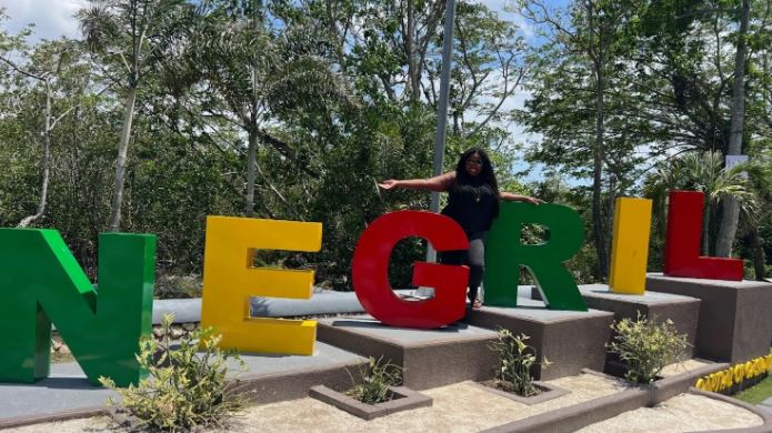 a woman is standing in front of a sign that says negril .