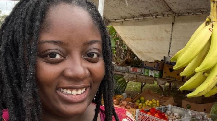 a woman with dreadlocks is smiling in front of a fruit stand .