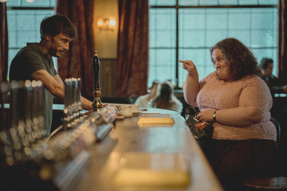 a man and a woman are sitting at a bar and the woman is pointing at the man