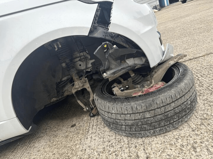 a white car with a damaged fender and tire