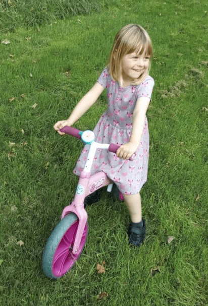 a little girl is riding a pink balance bike in the grass .