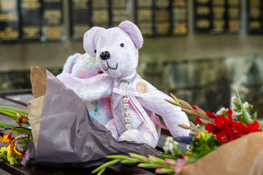 a pink teddy bear sits next to a bouquet of flowers