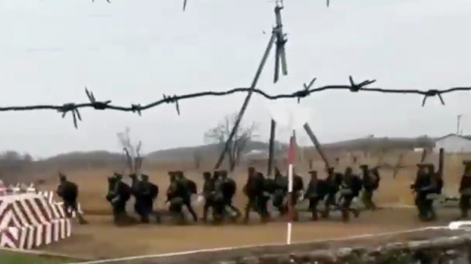 a group of soldiers are walking through a field behind barbed wire .