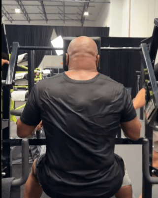 a man in a black shirt sits on a machine in a gym