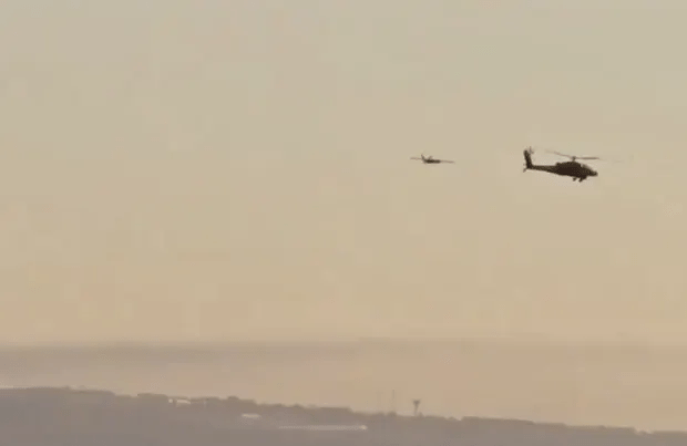 two helicopters are flying in the sky over a body of water .