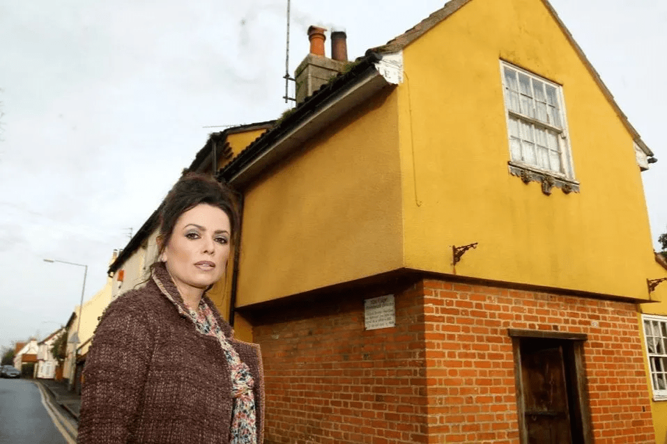 a woman stands in front of a yellow building that has a sign on it that says ' no parking '