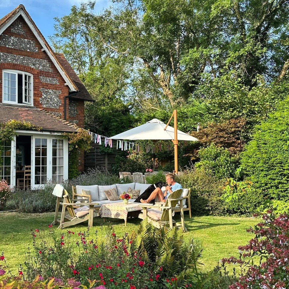 a woman sits on a couch under an umbrella in a garden