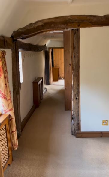 a long hallway in a house with wooden beams and a window .