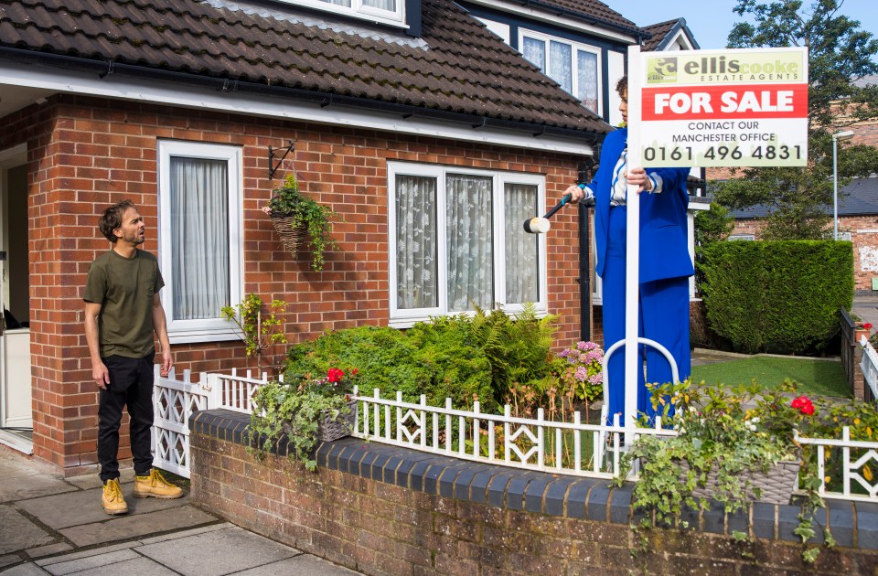 a man stands in front of a house with a for sale sign