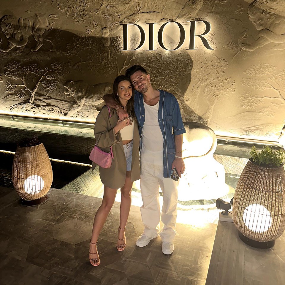 a man and woman pose in front of a dior sign