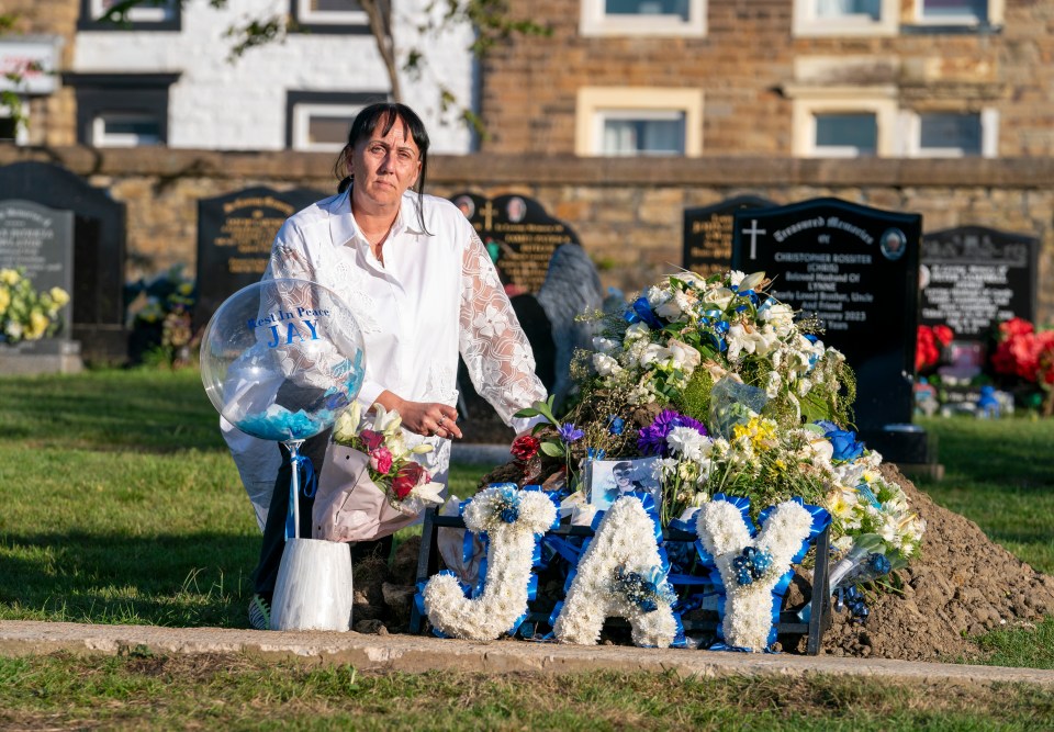 a woman kneeling in front of a grave with flowers and a sign that says jay