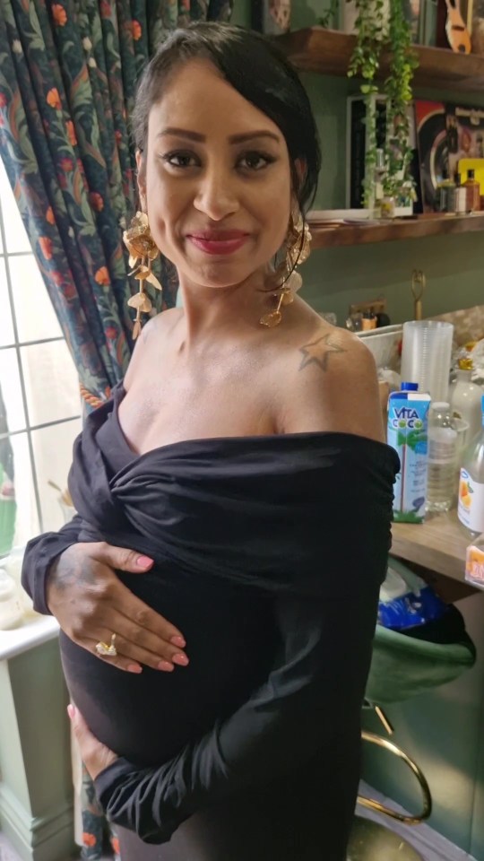 a woman in a black off the shoulder dress holds her belly