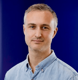 a man in a denim shirt is standing in front of a blue background