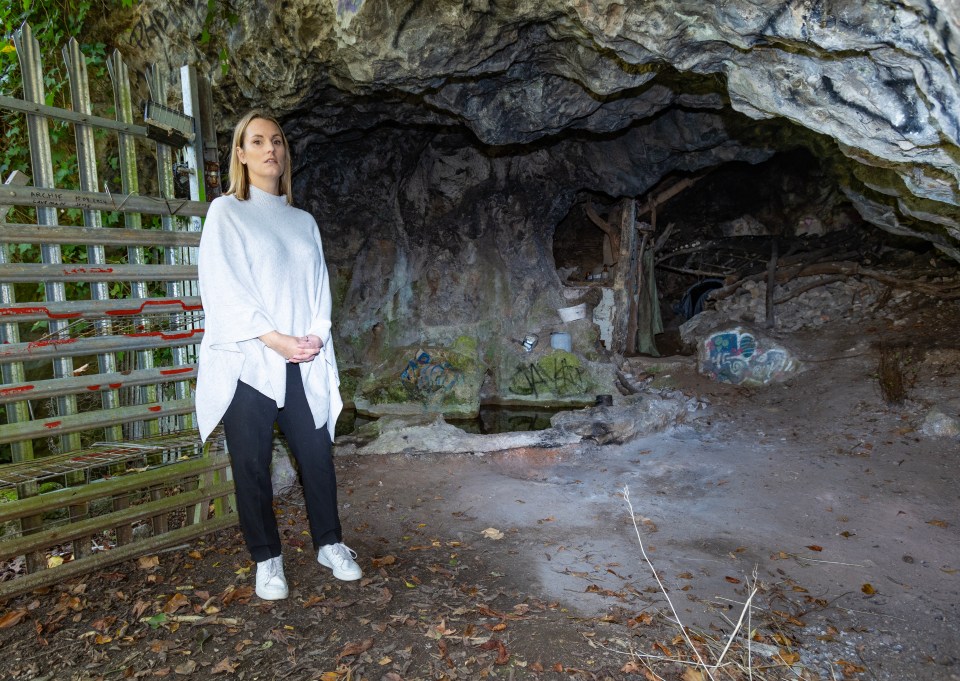 a woman in a white poncho stands in front of a cave